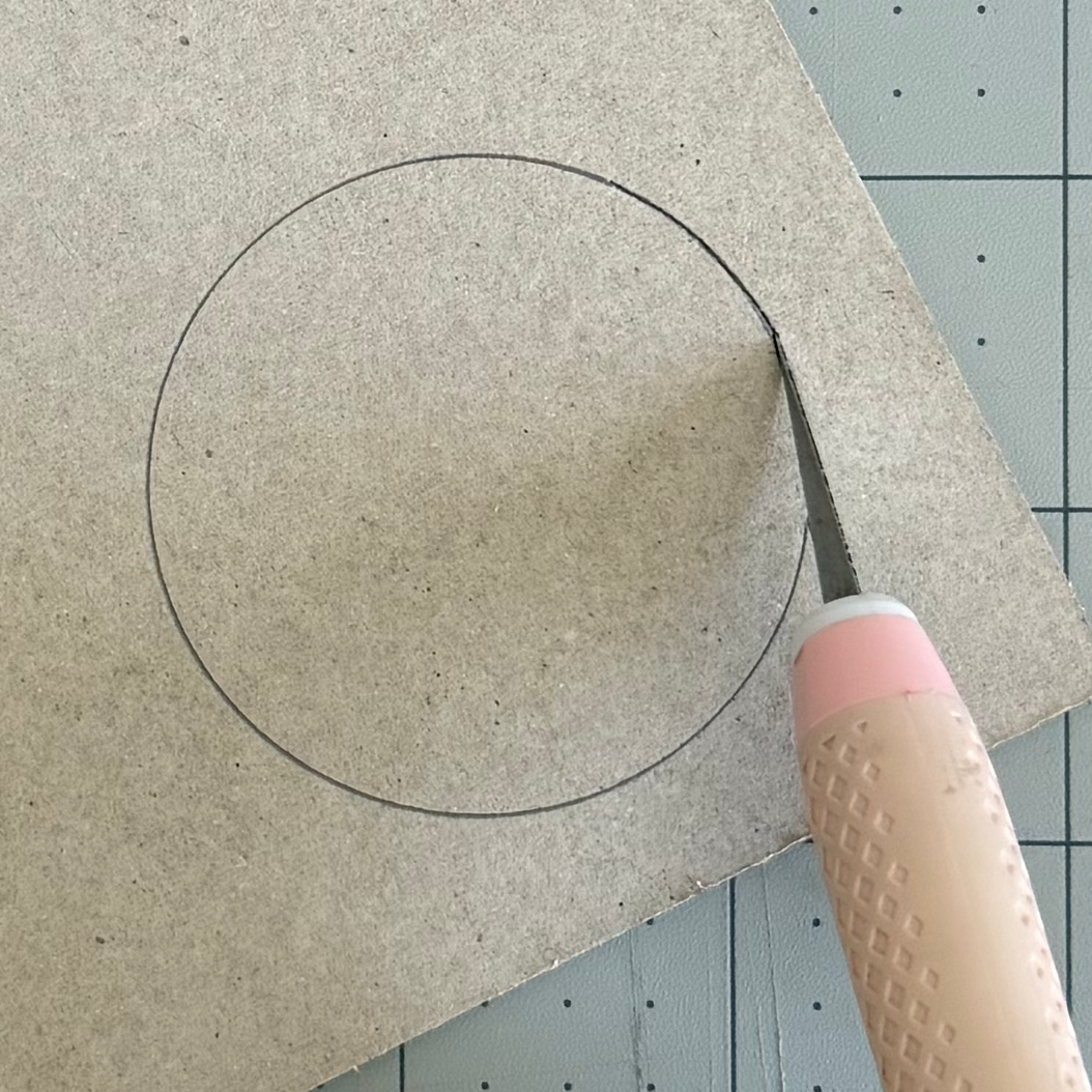 Beginning to cut a traced chipboard circle with a craft knife