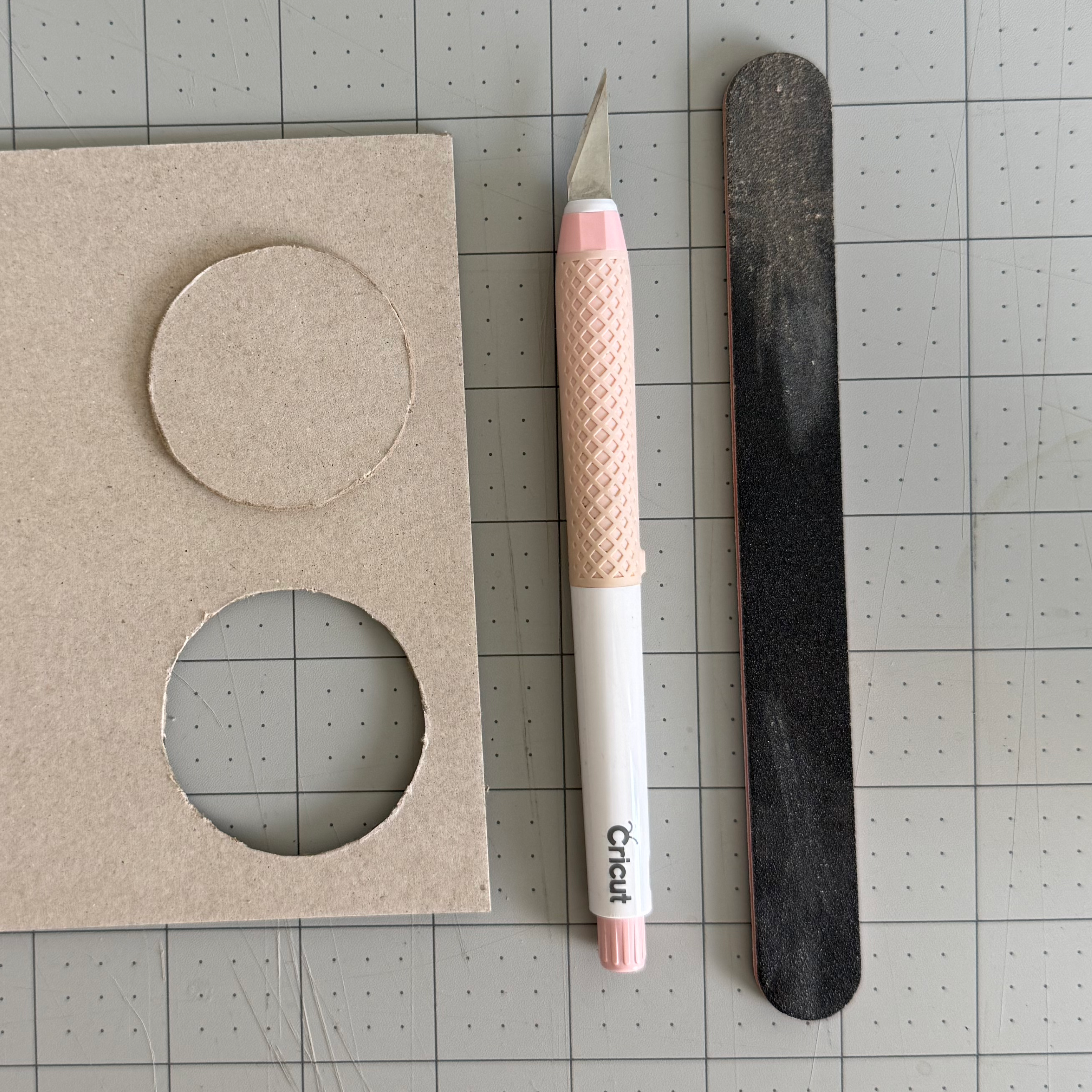 A craft knife and sanding file beside a smoothed chipboard circle
