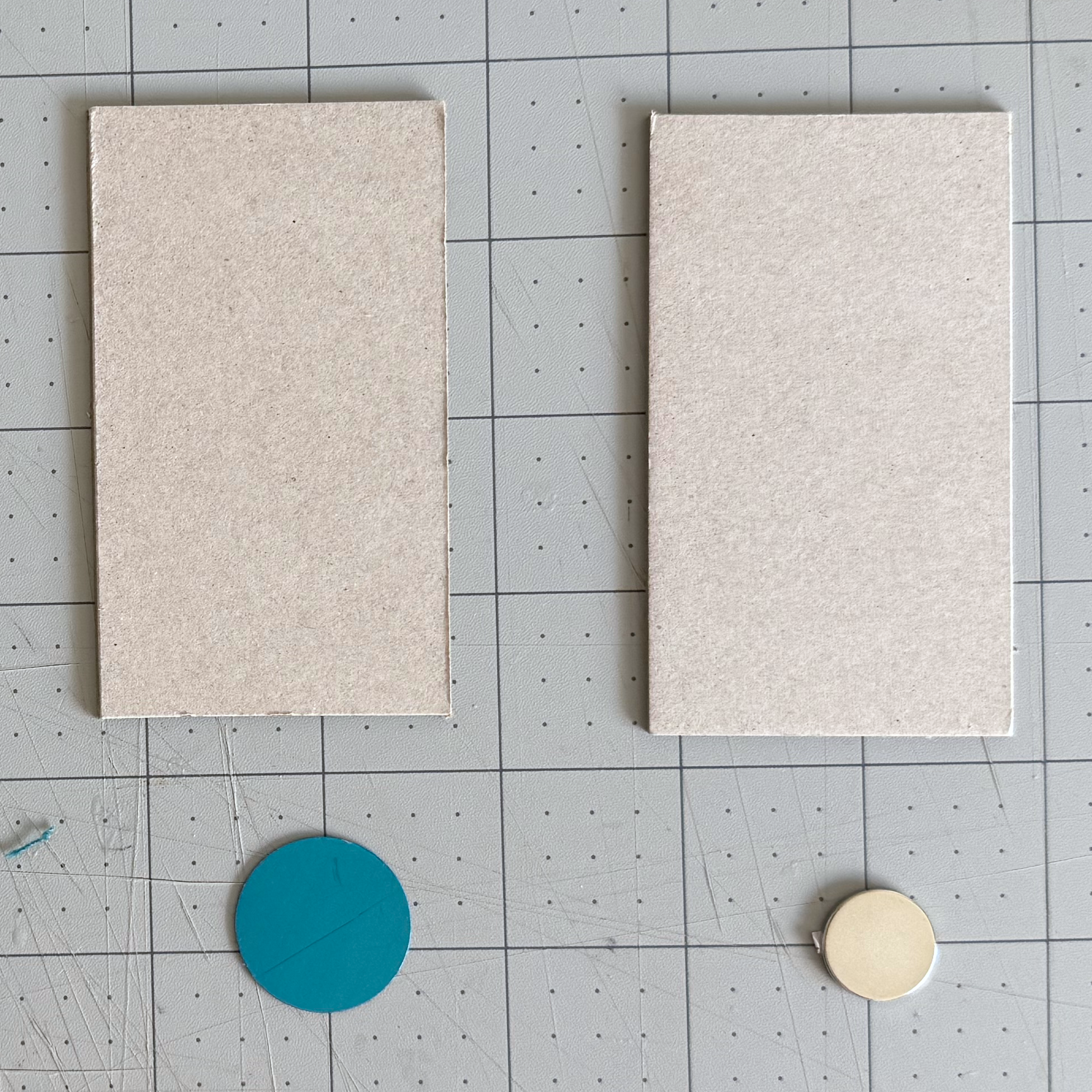 Magnet and larger metal disc beside their matching chipboard pieces